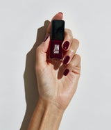 A hand holding a bottle nail polish in a deep burgundy shade