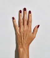 A close-up of a hand with manicured nails painted in a deep burgundy color, set against a plain light gray background