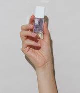 Hand holding a small clear bottle with a white cap against a plain background