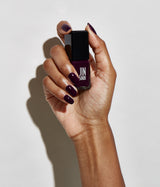 A hand holding a bottle of Jinsoon nail polish showing the deep plum-purple color on the nails