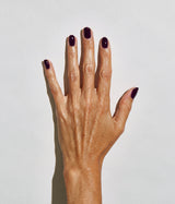 A close-up of a hand with manicured nails painted in a deep, glossy dark plum purple