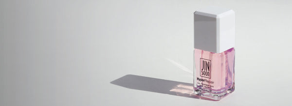 A pink nail polish repair container placed on the right side with soft light and shadows.