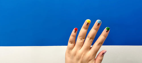 hand with colorful nails in front of blue wall 