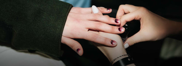 Hand with white nails holding a hand with a gradient nail design.