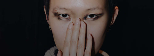 Asian model with dark make up, she covers her nose with her hand showing natural nails