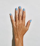 A close-up of a hand with light blue nail polish against a plain light gray background