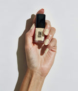 A hand holding a bottle of pale yellow nail polish against a clean white background with a strong shadow