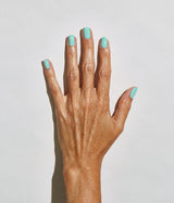 A close-up of a hand with a matte mint green nail polish, shown against a plain light gray background