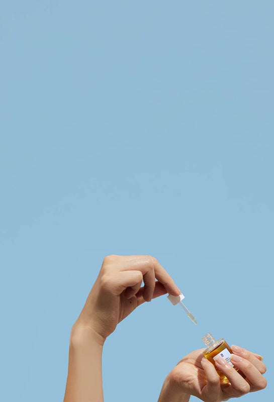 Hand holding a dropper with a small bottle against a light blue background
