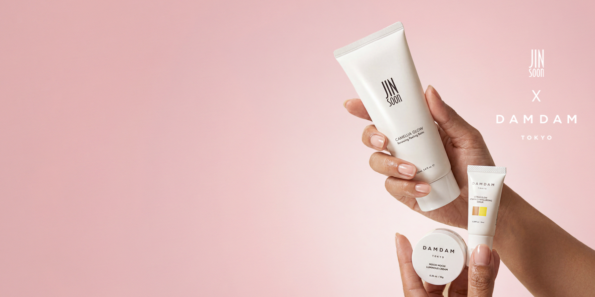 Hand holding skincare products with 'DAMDAM' branding on a pink background